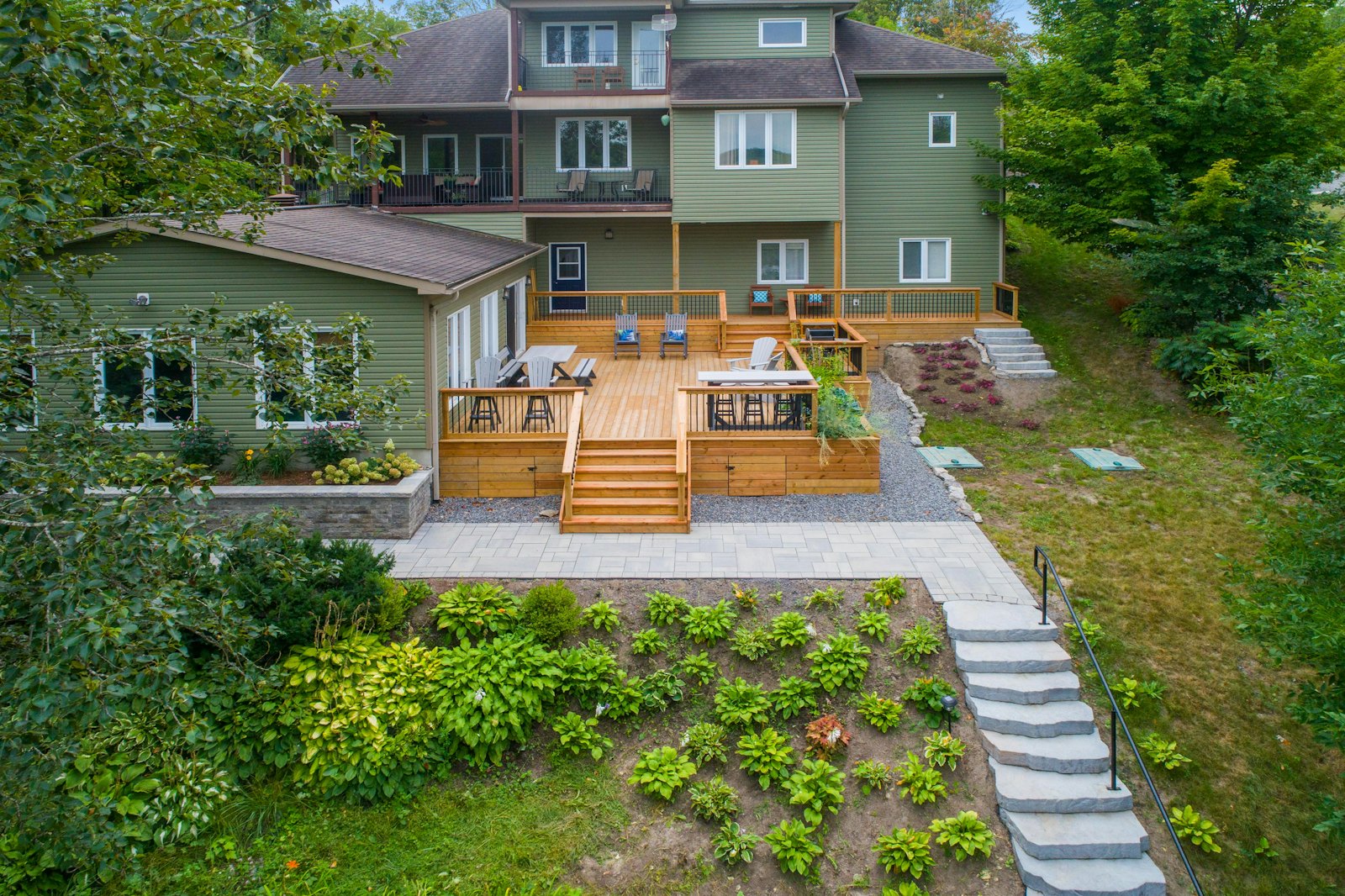 Terrasse en bois, dallage et escalier en pierre dans un jardin en pente